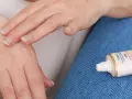 Mani che si toccano, alleviando rossore e prurito tra le dita. Accanto, un tubetto di crema Nivea.