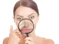 Donna osserva il suo naso con una lente d'ingrandimento, cercando di capire perché i punti neri puzzano.