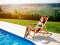 Donna rilassata su una sdraio accanto alla piscina, godendosi il sole per come abbronzarsi velocemente a casa. Paesaggio collinare sullo sfondo.