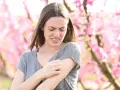 Donna con prurito in tutto il corpo, graffiandosi il braccio tra i fiori rosa.