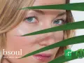 Occhi azzurri e pelle luminosa di una donna, con foglie verdi che creano un effetto di trasparenza, suggerendo un approccio naturale contro l'invecchiamento precoce.