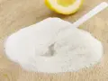 Polvere bianca, forse acido citrico, con un cucchiaino e una fetta di limone sullo sfondo. Ideale per la vitamina C.