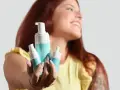 Donna sorridente mostra prodotti per skincare mattina: mousse detergente e siero.