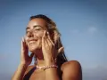 Donna sorridente applica crema solare per proteggere la pelle da macchie e tumore.