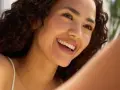 Donna sorridente con riccioli scuri, un esempio di come avere un viso più bello con un sorriso radioso e una pelle luminosa.