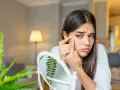 Ragazza preoccupata si tocca un brufolo sul viso, riflettendosi in uno specchio. La tentazione di schiacciarli è forte, ma la cura della pelle è importante.