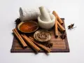 Ingredienti per una maschera al miele antirughe: miele dorato, cannella, anice stellato, mortaio e asciugamano arrotolato.