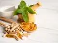 Cucchiaio con capsule e pillole, tra cui quelle contenenti tocoferolo dove si trova, accanto a un mortaio con menta.