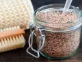 Un barattolo di scrub miele e zucchero, con una spazzola e una spugna per il corpo.