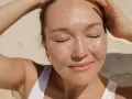 Donna con lentiggini al sole, con le mani tra i capelli. Forse la crema solare tutti i giorni fa male?