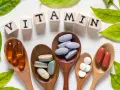 Cucchiaini di legno pieni di pillole e capsule, con le lettere che compongono la parola "VITAMIN" e foglie verdi. Tra le pillole, si nota la vitamina b6.