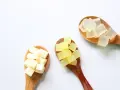 Tre cucchiai di legno con cubetti di sapone trasparente, giallo e bianco. La glicerina da dove si ricava è un ingrediente chiave per questi saponi.