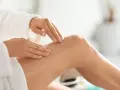 Mani che applicano body scrub sulla gamba, un gesto delicato per una pelle liscia. Scopri come si usa il body scrub per un trattamento efficace.