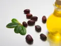 Semi di jojoba e una bottiglia di olio dorato, evidenziando le proprietà dell'olio di jojoba per la cura della pelle.