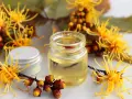 Un flacone di olio giallo circondato da fiori di amamelide, che mostra cos'è questa pianta benefica.