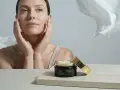Donna con mani sul viso, vicino a un vasetto di crema. Soluzione per pelle secca viso rimedi.