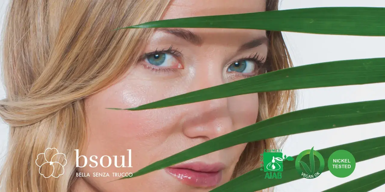 Occhi azzurri e pelle luminosa di una donna, con foglie verdi che creano un effetto di trasparenza, suggerendo un approccio naturale contro l'invecchiamento precoce.