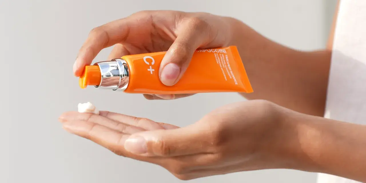 Mani che dosano crema viso con vitamina C, per illuminare e proteggere la pelle.