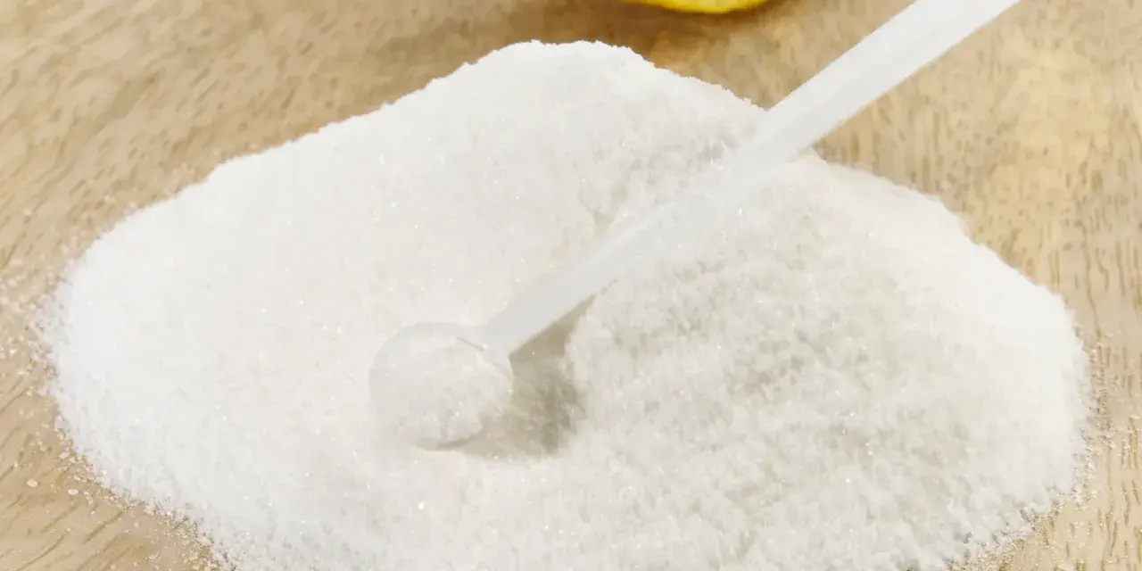 Polvere bianca, forse acido citrico, con un cucchiaino e una fetta di limone sullo sfondo. Ideale per la vitamina C.