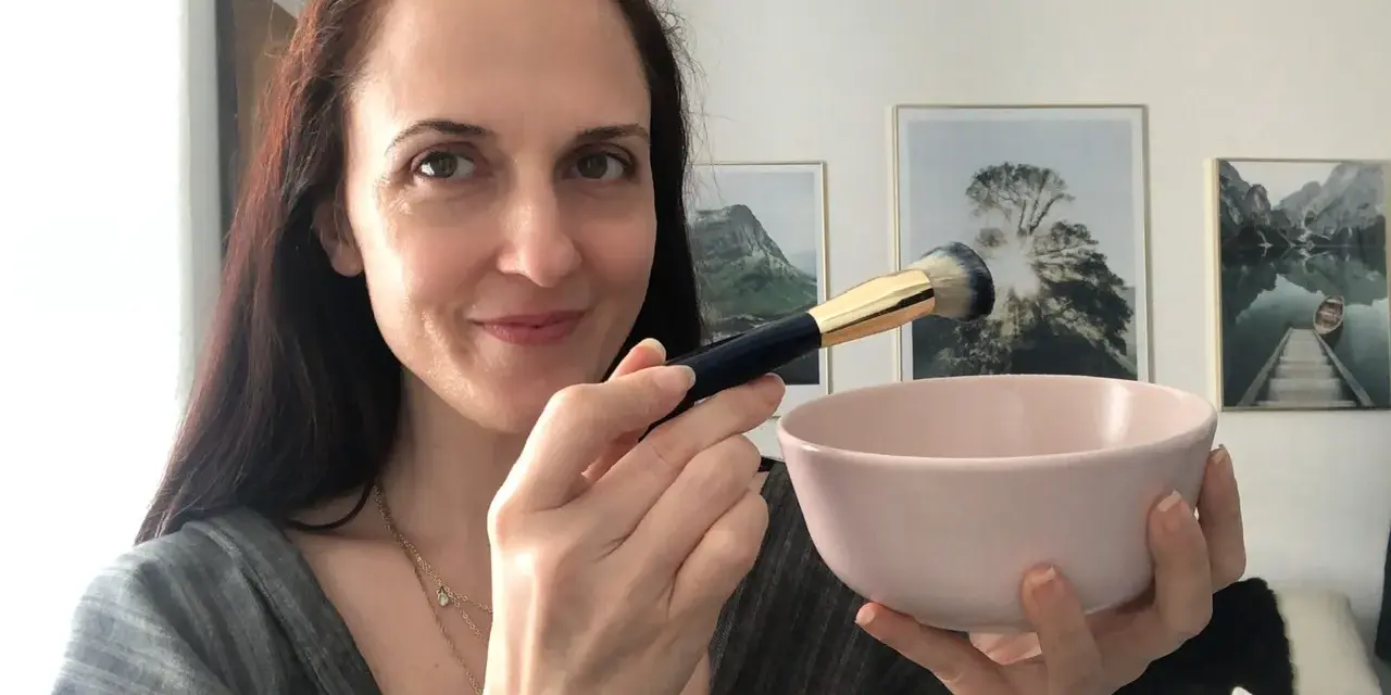Donna prepara una maschera viso fai da te con bicarbonato, usando un pennello per applicarla.