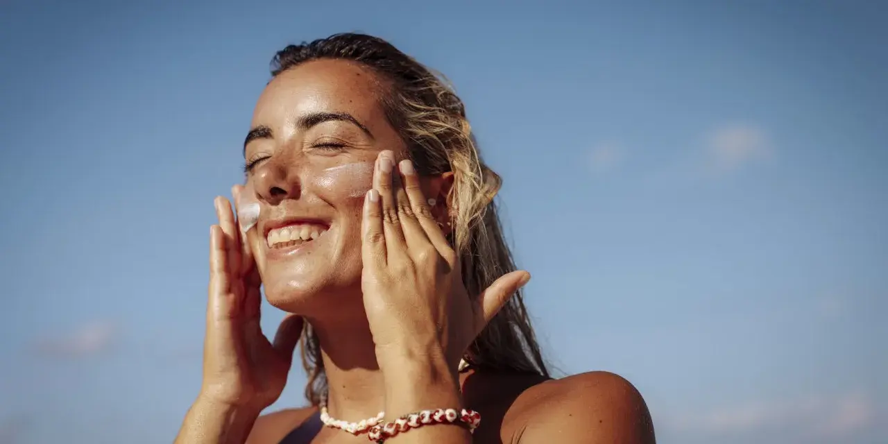 Donna sorridente applica crema solare per proteggere la pelle da macchie e tumore.