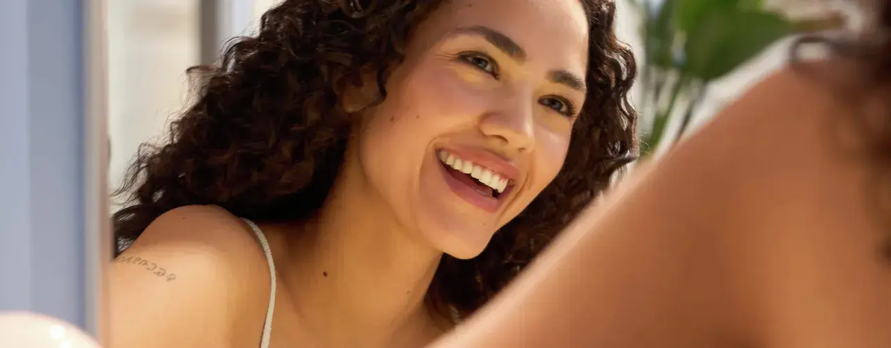 Donna sorridente con riccioli scuri, un esempio di come avere un viso più bello con un sorriso radioso e una pelle luminosa.