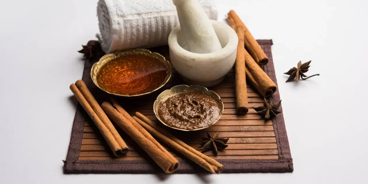 Ingredienti per una maschera al miele antirughe: miele dorato, cannella, anice stellato, mortaio e asciugamano arrotolato.