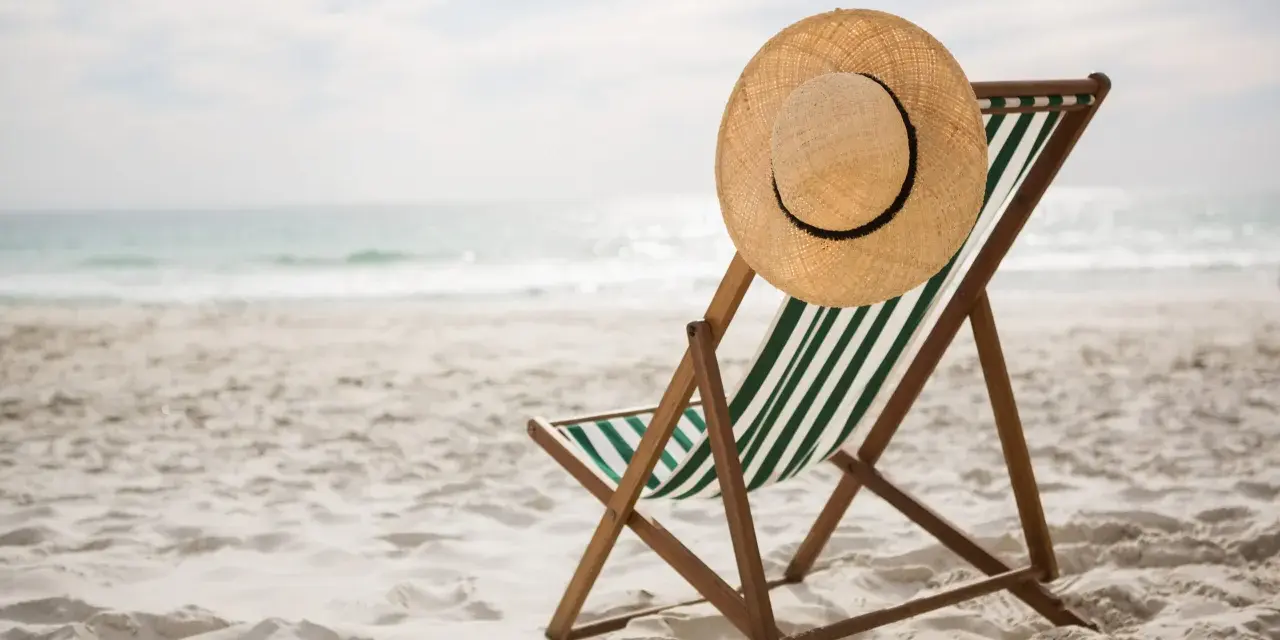 Spiaggia deserta con sdraio e cappello di paglia. Ricorda i rimedi per il colpo di calore: idratarsi e cercare l'ombra.