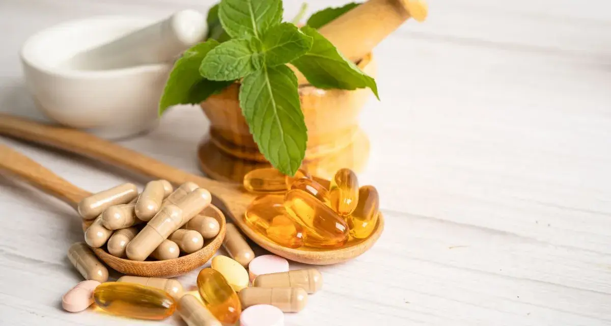 Cucchiaio con capsule e pillole, tra cui quelle contenenti tocoferolo dove si trova, accanto a un mortaio con menta.