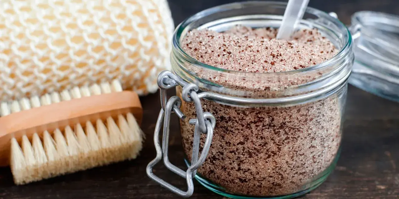 Un barattolo di scrub miele e zucchero, con una spazzola e una spugna per il corpo.