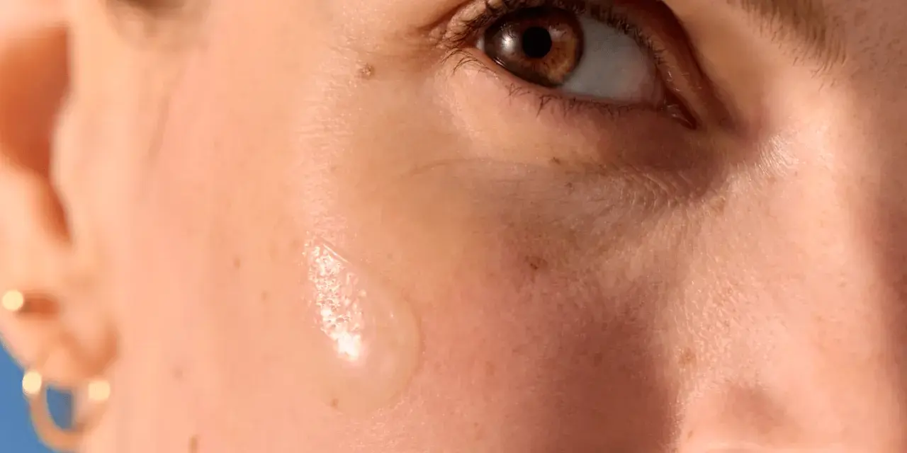 Goccia di siero su pelle abbronzata con delicati puntini bianchi visibili.