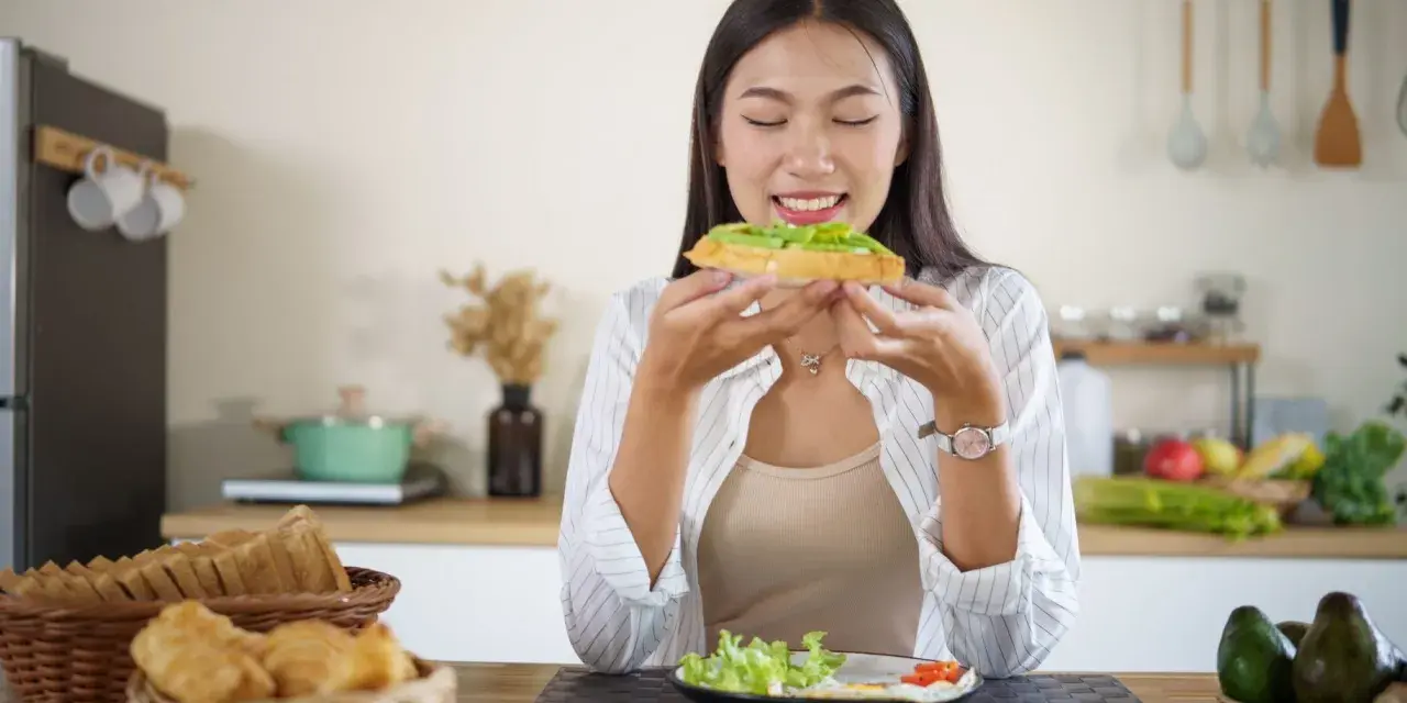 Donna assapora un toast con avocado, un alimento ricco di vitamina E, essenziale per la pelle e il sistema immunitario.