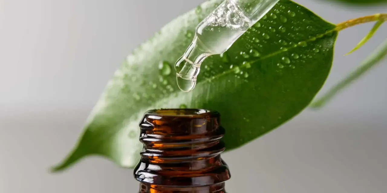 Goccia di liquido trasparente da un contagocce su una foglia verde bagnata. Il contagocce è sopra una bottiglietta di vetro ambrato. Cos'è il glicerolo?