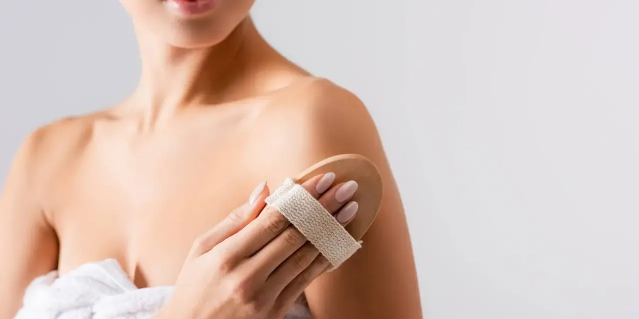 Donna usa una spazzola per il corpo per esfoliare la pelle, un segreto per come mantenere abbronzatura a lungo.