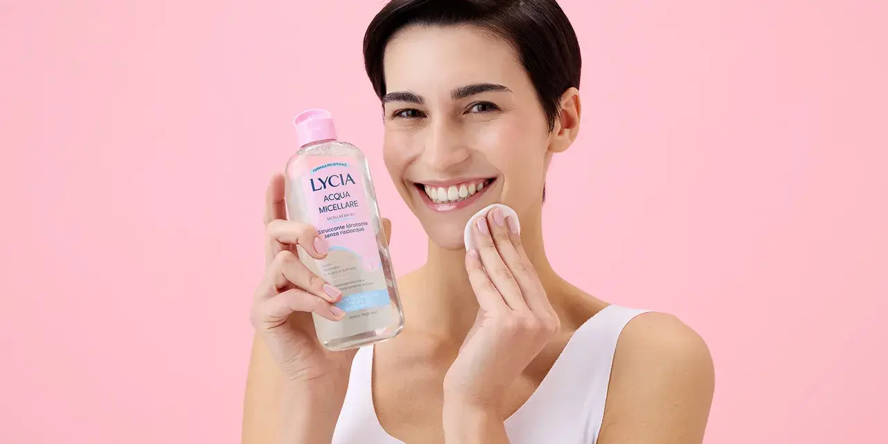 Donna sorridente con acqua micellare Lycia e dischetto di cotone, perfetta per imparare come pulire il viso quotidianamente.