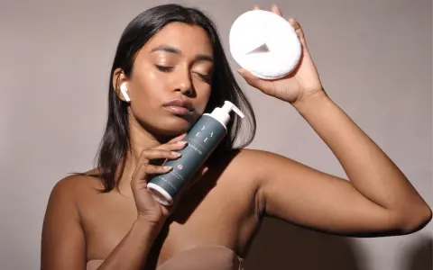 Donna con latte detergente e dischetto struccante, pronta per la pulizia del viso dopo il latte detergente il viso va lavato.