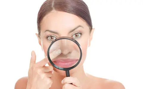 Donna osserva il suo naso con una lente d'ingrandimento, cercando di capire perché i punti neri puzzano.