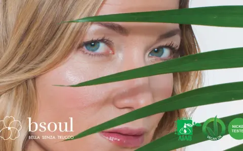 Occhi azzurri e pelle luminosa di una donna, con foglie verdi che creano un effetto di trasparenza, suggerendo un approccio naturale contro l'invecchiamento precoce.