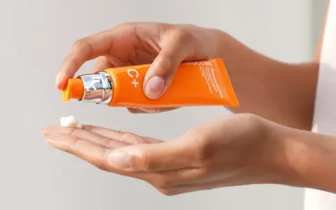 Mani che dosano crema viso con vitamina C, per illuminare e proteggere la pelle.