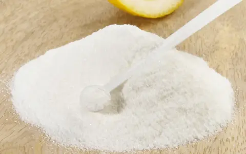 Polvere bianca, forse acido citrico, con un cucchiaino e una fetta di limone sullo sfondo. Ideale per la vitamina C.