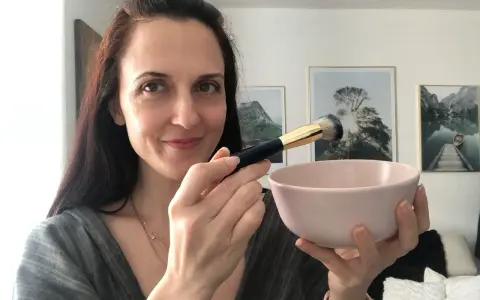 Donna prepara una maschera viso fai da te con bicarbonato, usando un pennello per applicarla.