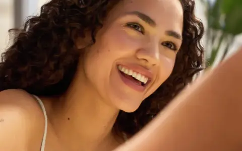 Donna sorridente con riccioli scuri, un esempio di come avere un viso più bello con un sorriso radioso e una pelle luminosa.