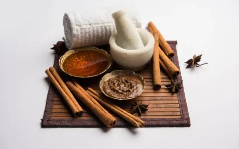 Ingredienti per una maschera al miele antirughe: miele dorato, cannella, anice stellato, mortaio e asciugamano arrotolato.