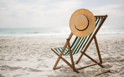 Spiaggia deserta con sdraio e cappello di paglia. Ricorda i rimedi per il colpo di calore: idratarsi e cercare l'ombra.