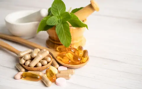 Cucchiaio con capsule e pillole, tra cui quelle contenenti tocoferolo dove si trova, accanto a un mortaio con menta.