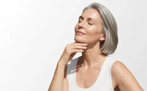 Donna con capelli grigi e pelle luminosa, che accarezza il collo. Scopri i migliori rimedi per le rughe del collo.