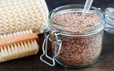 Un barattolo di scrub miele e zucchero, con una spazzola e una spugna per il corpo.