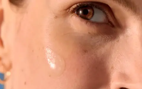 Goccia di siero su pelle abbronzata con delicati puntini bianchi visibili.
