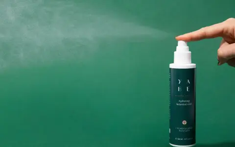 Dito come si usa il tonico viso: una mano spruzza il tonico idratante YABE su sfondo verde.