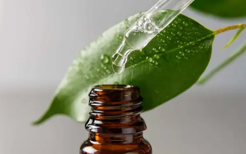 Goccia di liquido trasparente da un contagocce su una foglia verde bagnata. Il contagocce è sopra una bottiglietta di vetro ambrato. Cos'è il glicerolo?